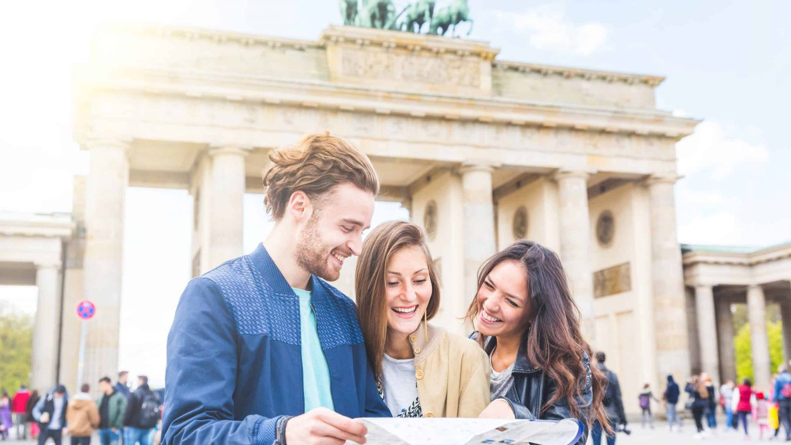 Multiracial group of friends visiting the city of Berlin. Two women and a man looking at a map with Brandenburg Gate on background. Lifestyle, friendship and tourism concepts with real people models.
