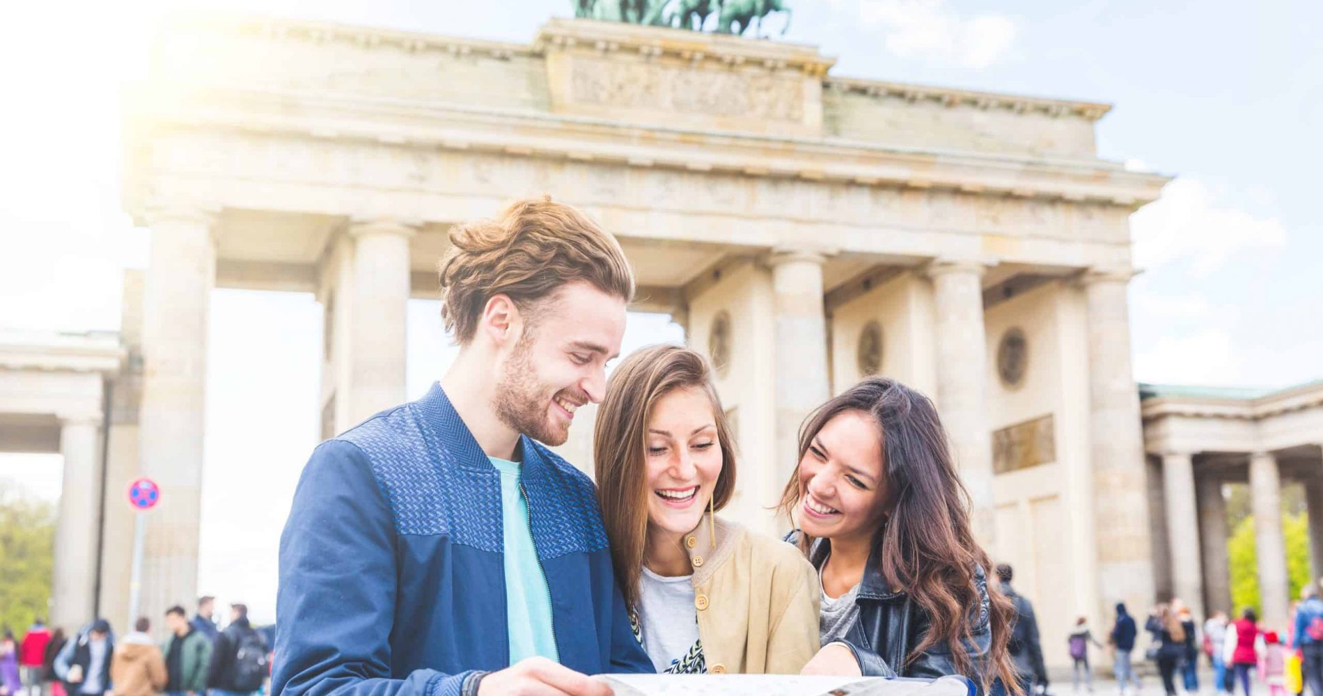 Multiracial group of friends visiting the city of Berlin. Two women and a man looking at a map with Brandenburg Gate on background. Lifestyle, friendship and tourism concepts with real people models.